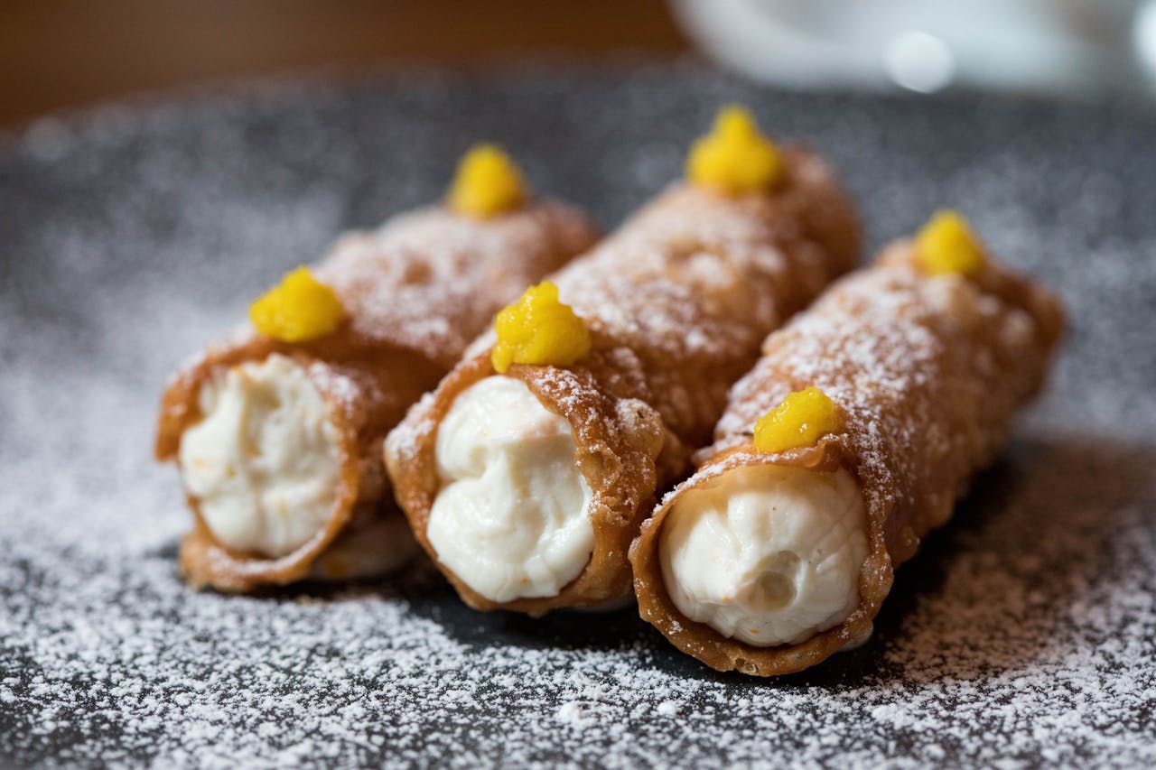 Three fresh Italian cannolis with cream filling and powdered sugar.